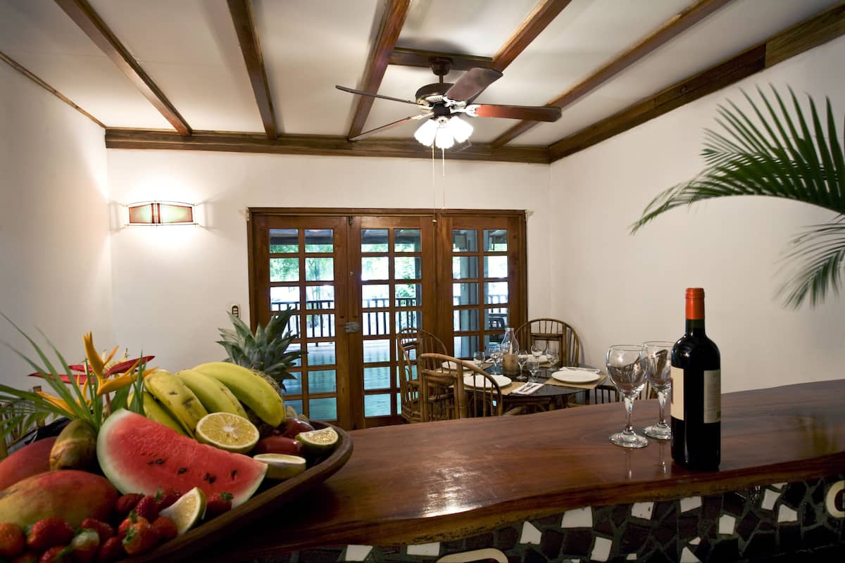 Un comedor con una mesa de madera, sillas, un frutero, una botella de vino y un ventilador de techo.