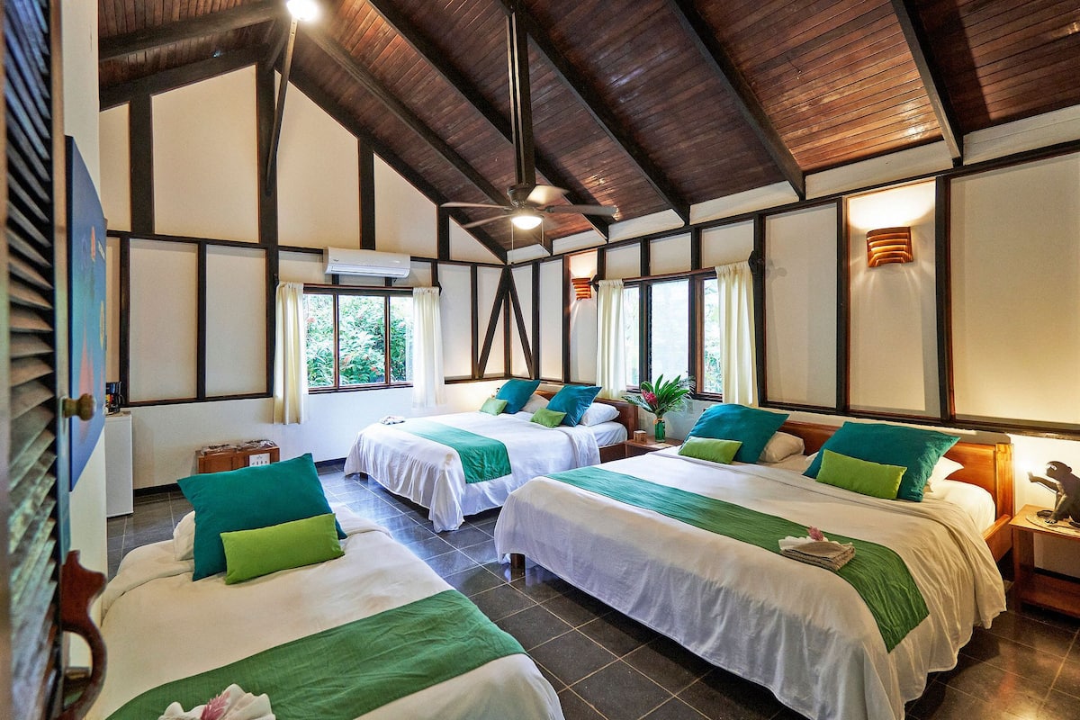 Habitación de hotel con dos camas, ventilador de techo y ventana con cortinas.