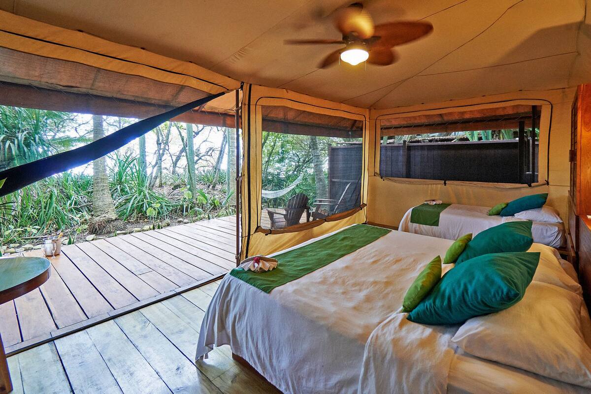 Una habitación con dos camas, ventilador de techo y una hamaca.