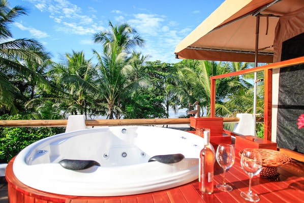 A hot tub on a wooden deck with a view of palm trees and a beach. - Hotel Tropico Latino (Cóbano)