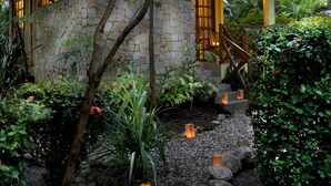 A stone house with a green roof, surrounded by lush greenery and a stone pathway with lanterns. - Hotel Tropico Latino (Cóbano)