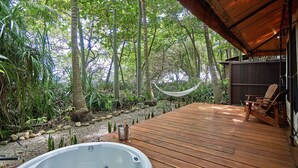 A wooden deck with a hot tub, a hammock, and a chair, surrounded by lush greenery. - Hotel Tropico Latino (Cóbano)
