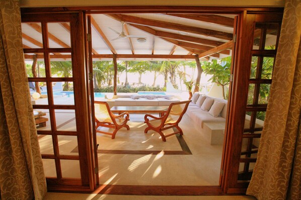 An open wooden door leading to a pool area with a sofa and two chairs. - Hotel Tropico Latino (Cóbano)