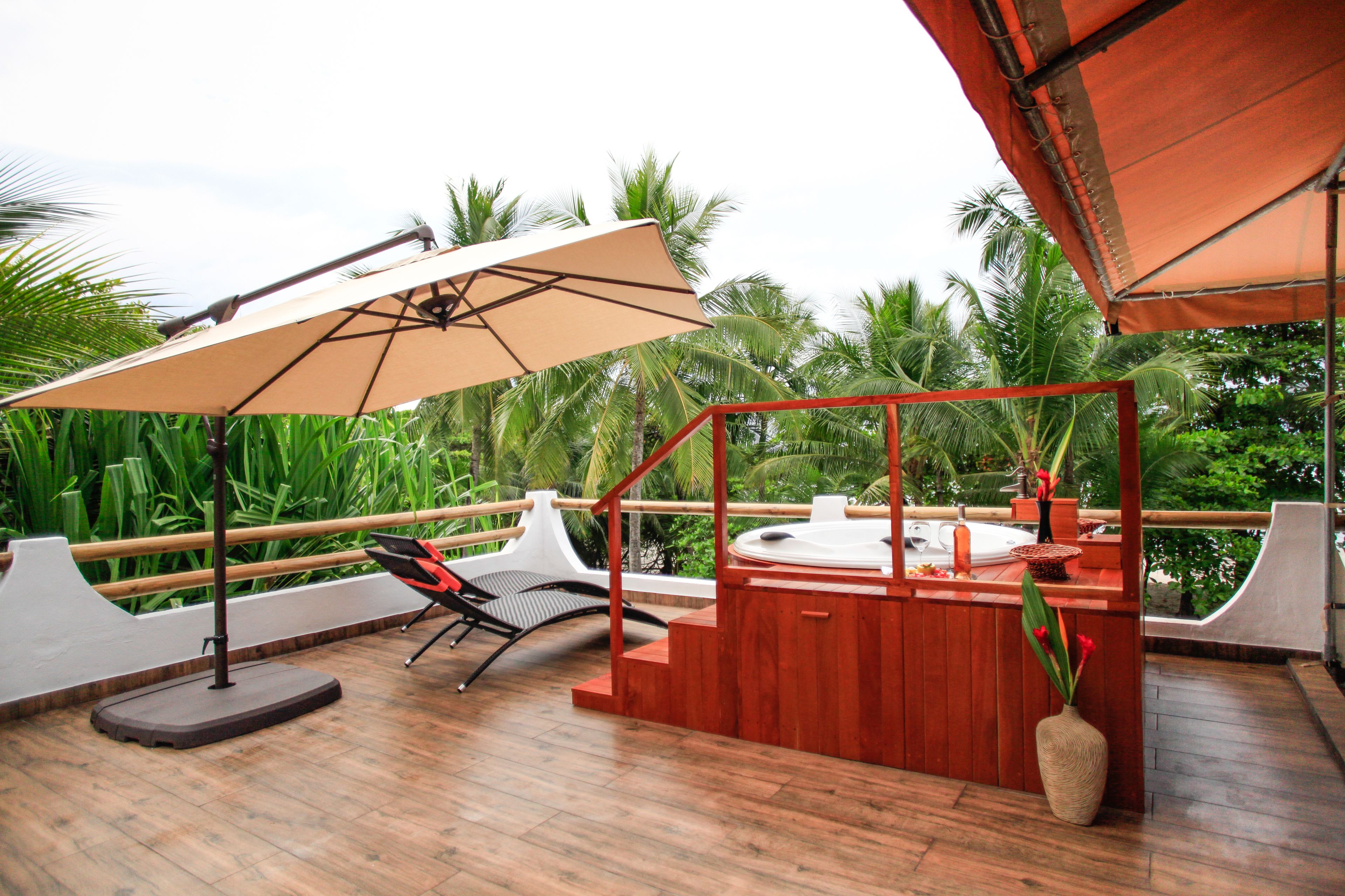 A wooden deck with a hot tub, a lounge chair, and a large umbrella providing shade.