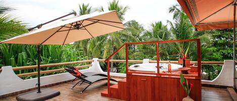 A wooden deck with a hot tub, a lounge chair, and a large umbrella providing shade.