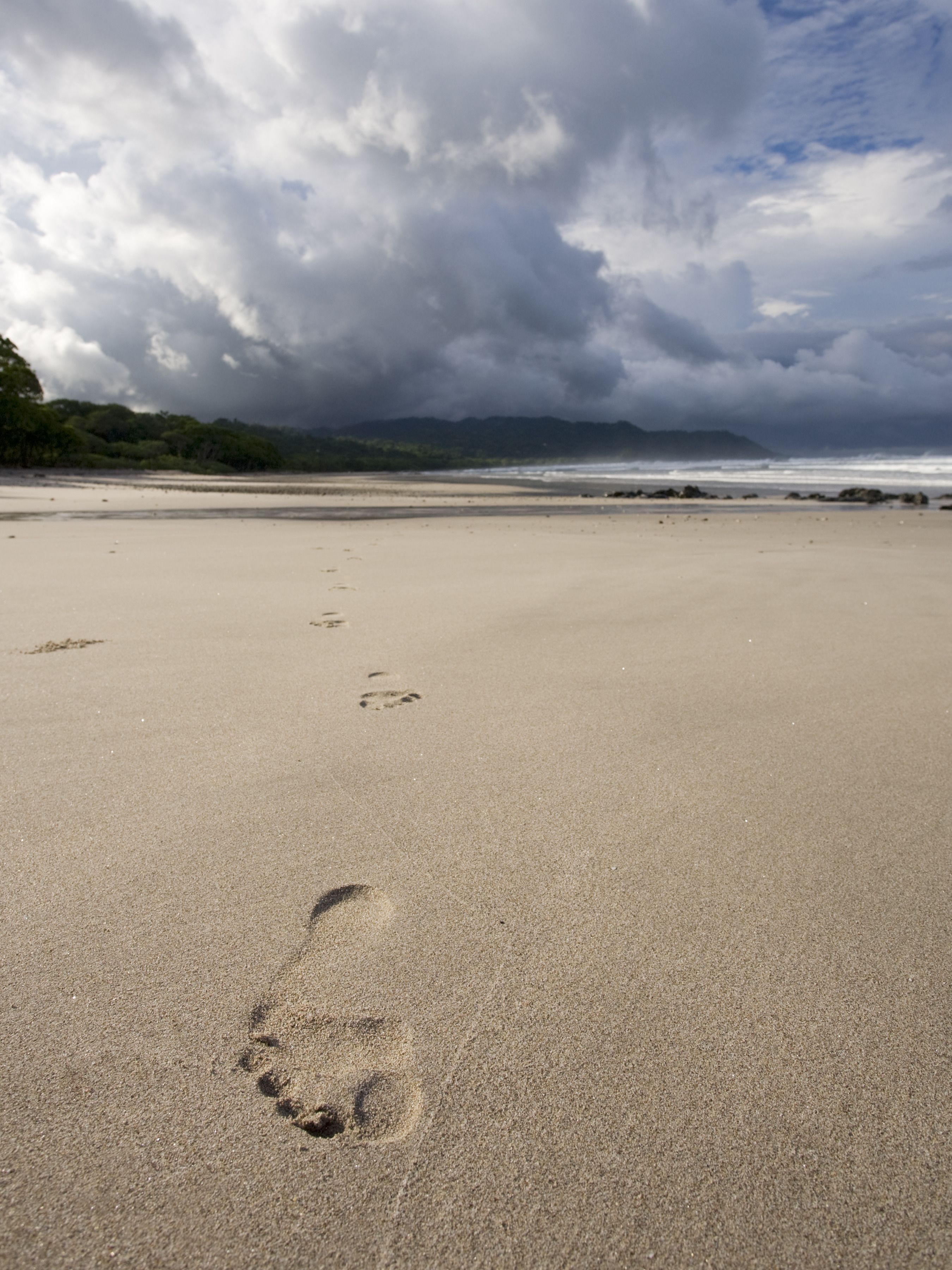 A beach with footprints in the sand and a cloudy sky.