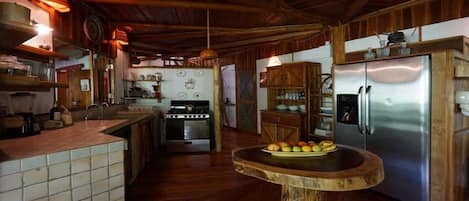 Una cocina rústica con armarios de madera, un refrigerador de acero inoxidable y una mesa redonda de madera con fruta.