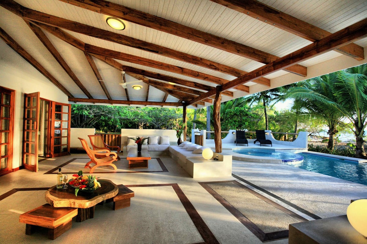 Un área de descanso al aire libre con piscina, muebles de madera y vistas al entorno verde.