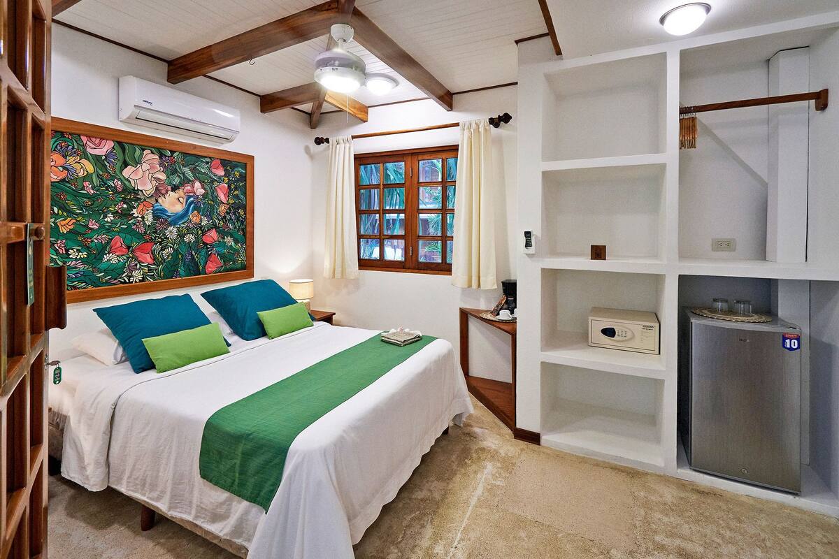 Un dormitorio con cama, ventana, un cuadro y un minibar.