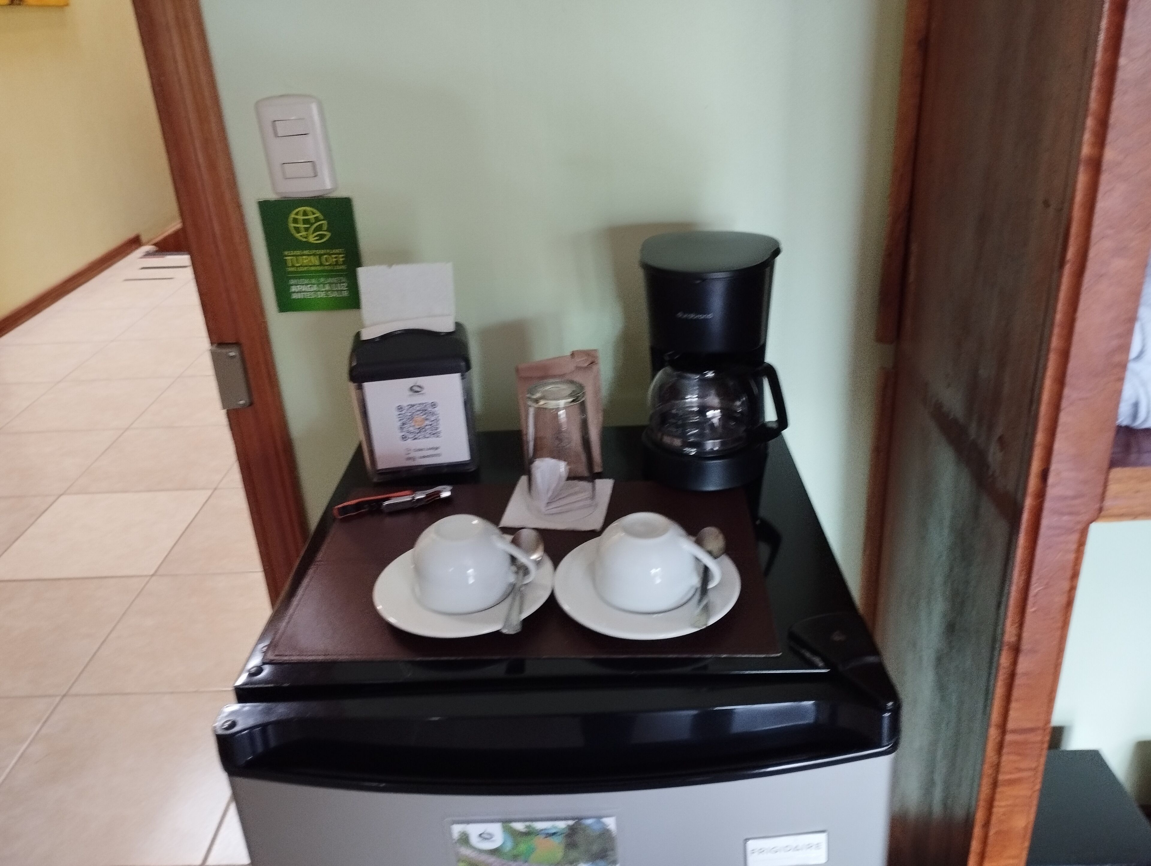 A hotel room with a coffee station featuring a coffee maker, cups, and a milk frother.