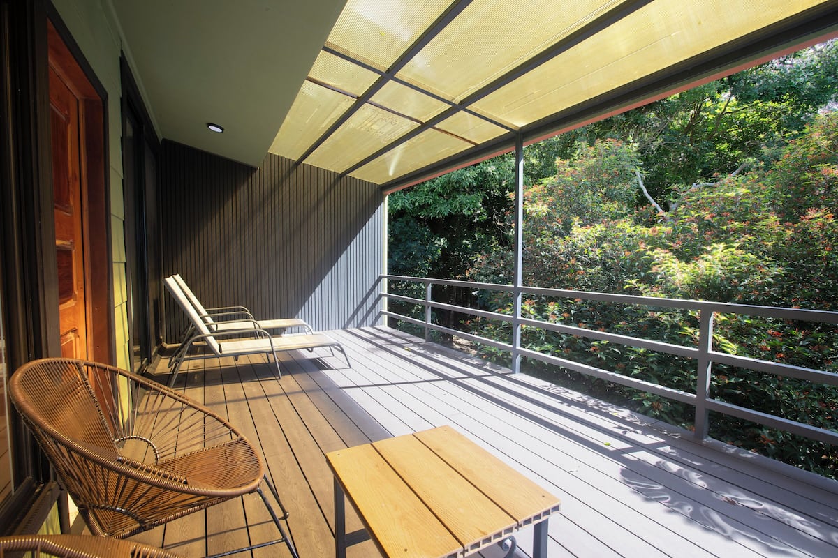 A wooden deck with a table and chairs, a glass railing, and a view of trees.