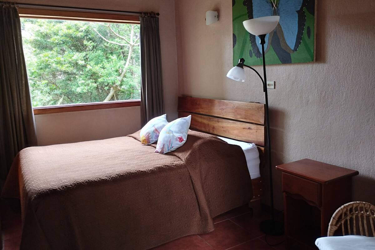 A bedroom with a bed, a nightstand, a lamp, a chair, and a painting of a butterfly.