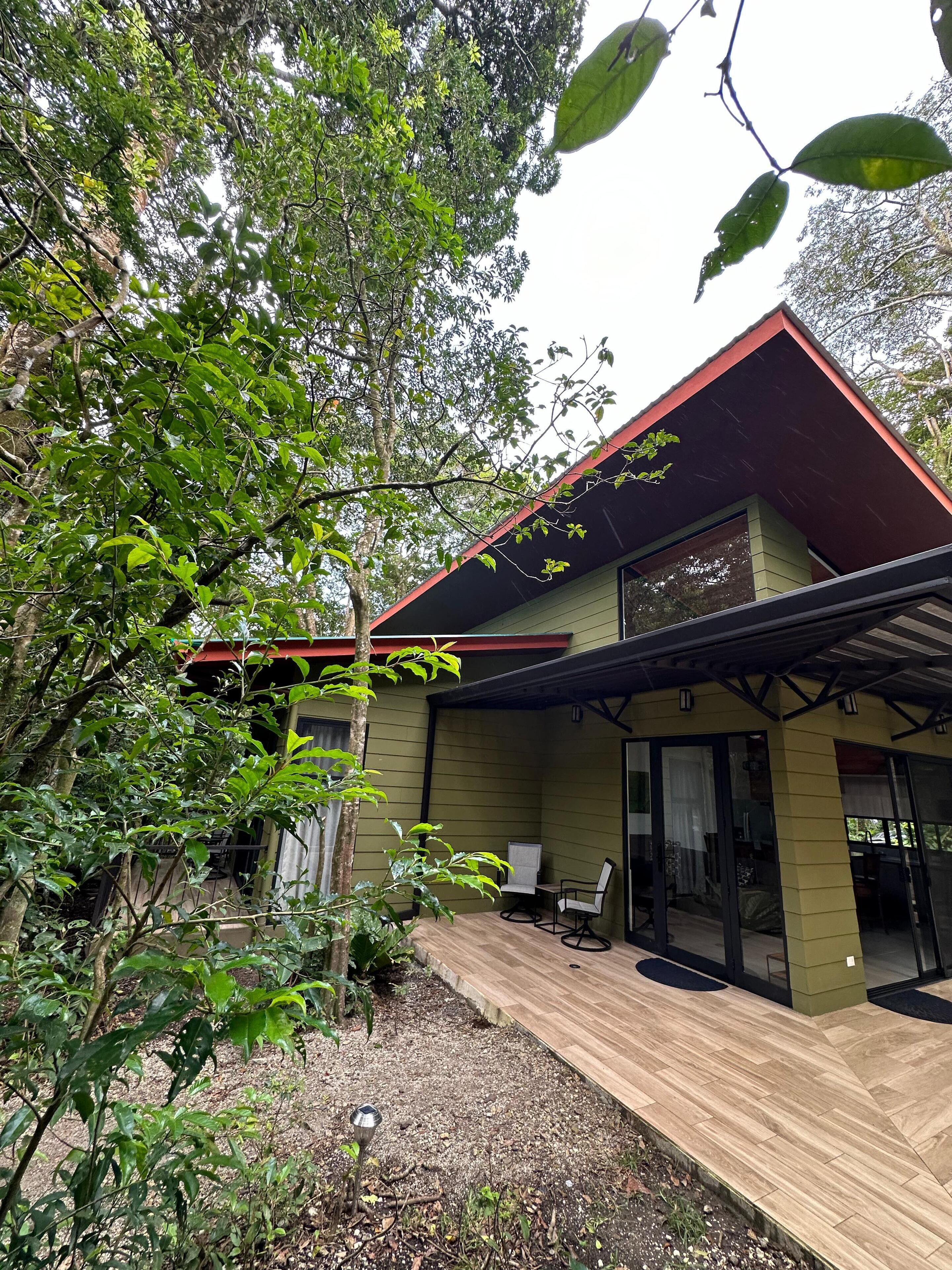 A modern house with a red roof, a covered patio, and a garden area with trees and plants.