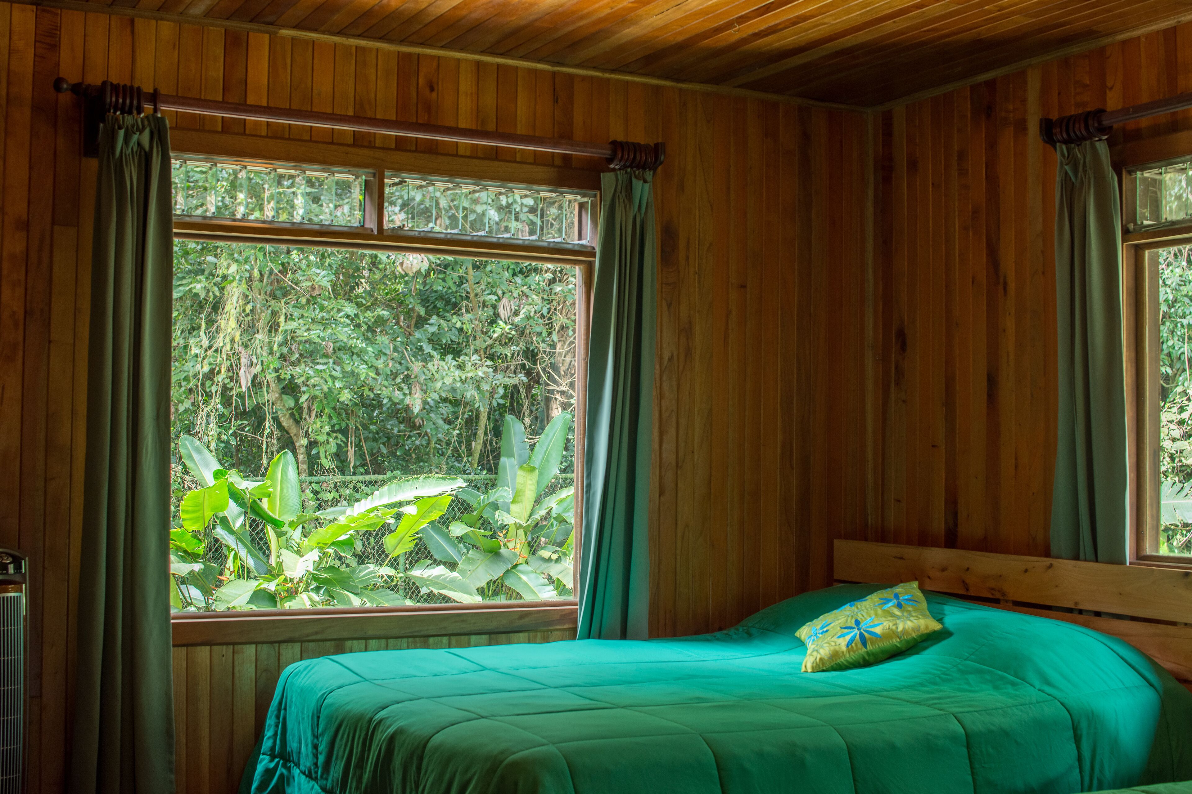 A wooden-paneled room with a bed, large windows, and curtains.