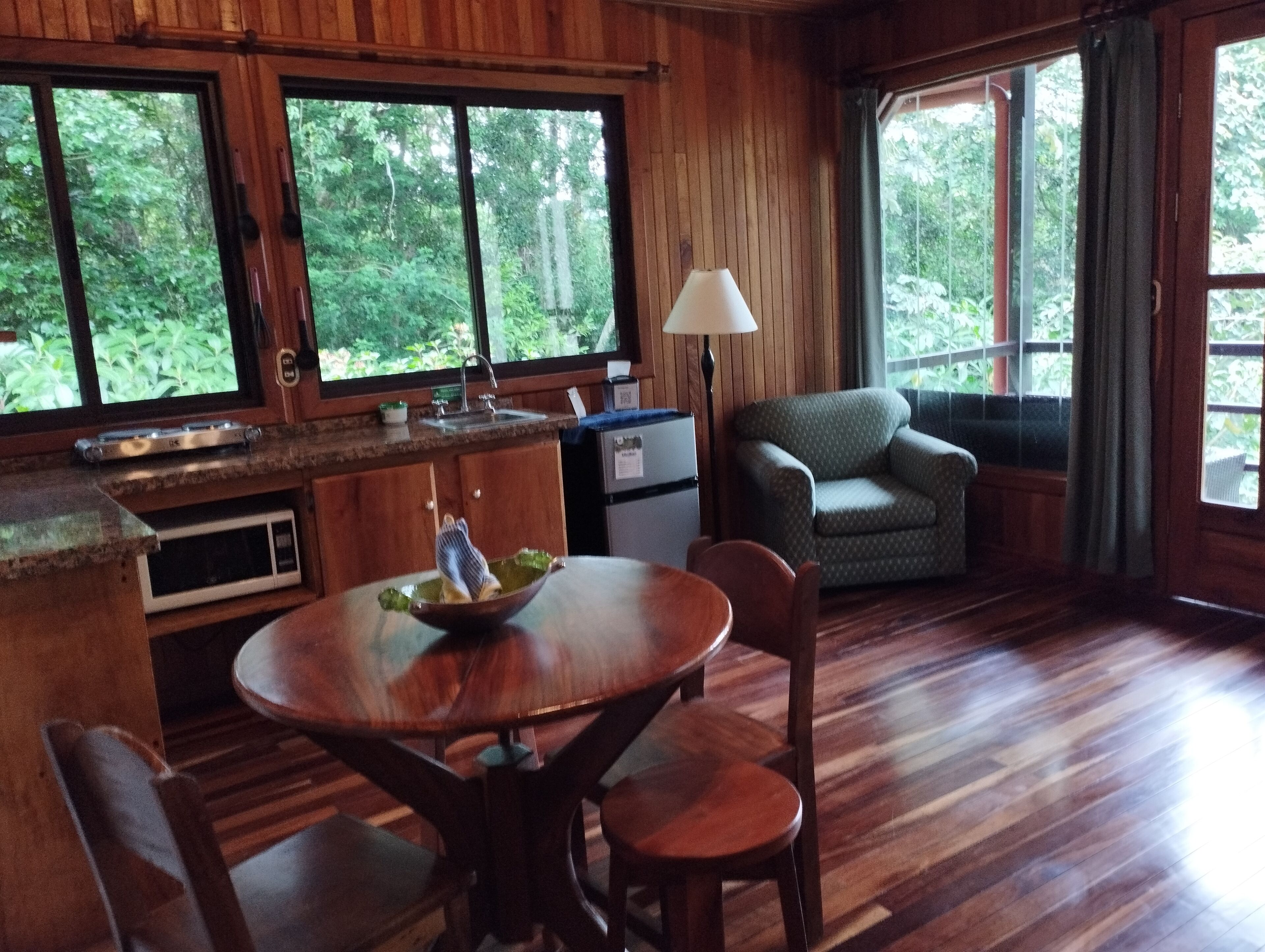 A wooden interior with a dining table, chairs, a sofa, and a lamp.