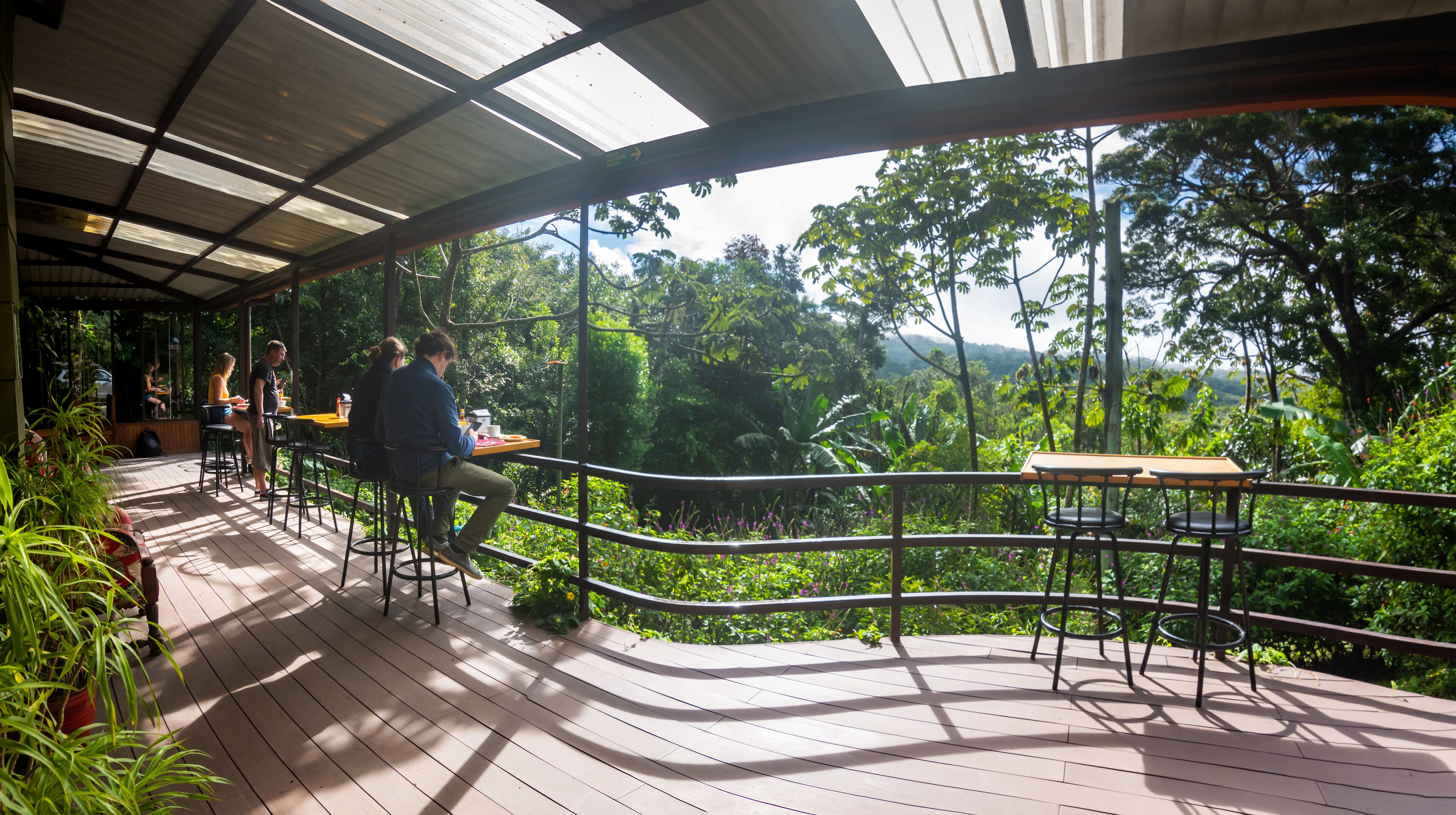An outdoor dining area with a wooden deck, metal railing, and tables.