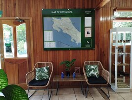 Interior em madeira com um mapa da Costa Rica na parede, cadeiras de vime com almofadas, uma pequena mesa com garrafas e uma vitrine de vidro.