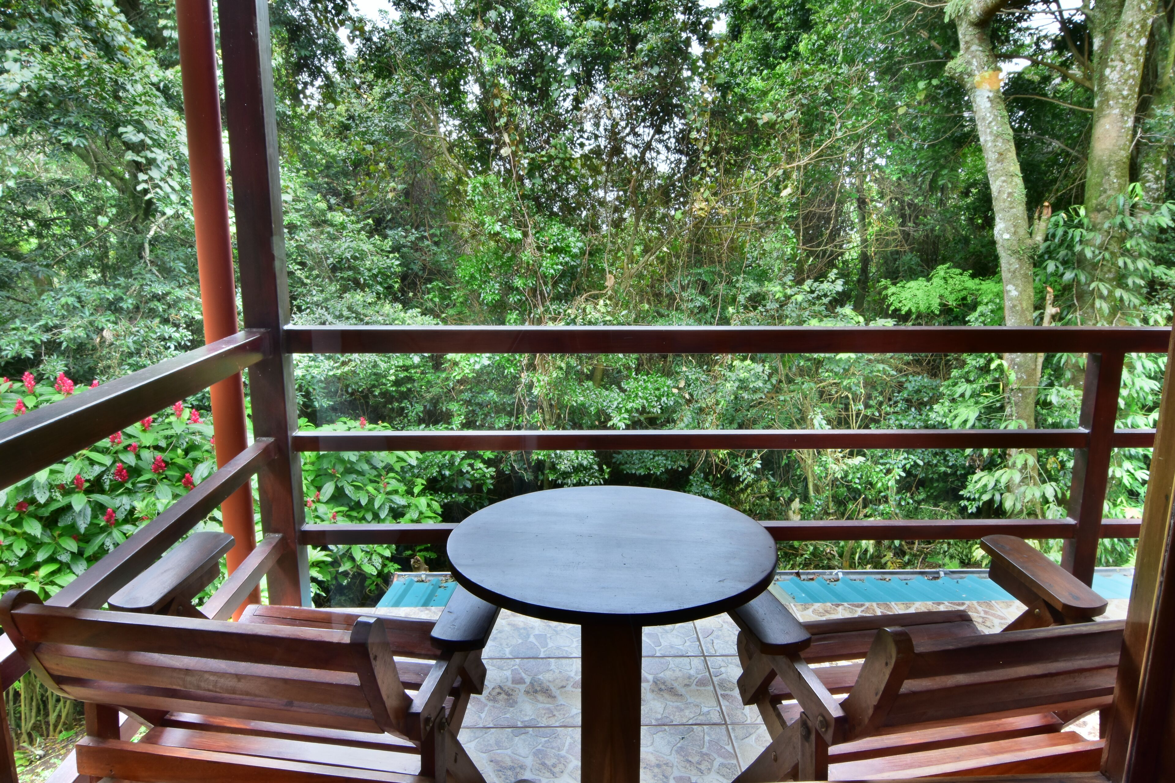 A wooden table and benches on a balcony with a view of dense greenery.