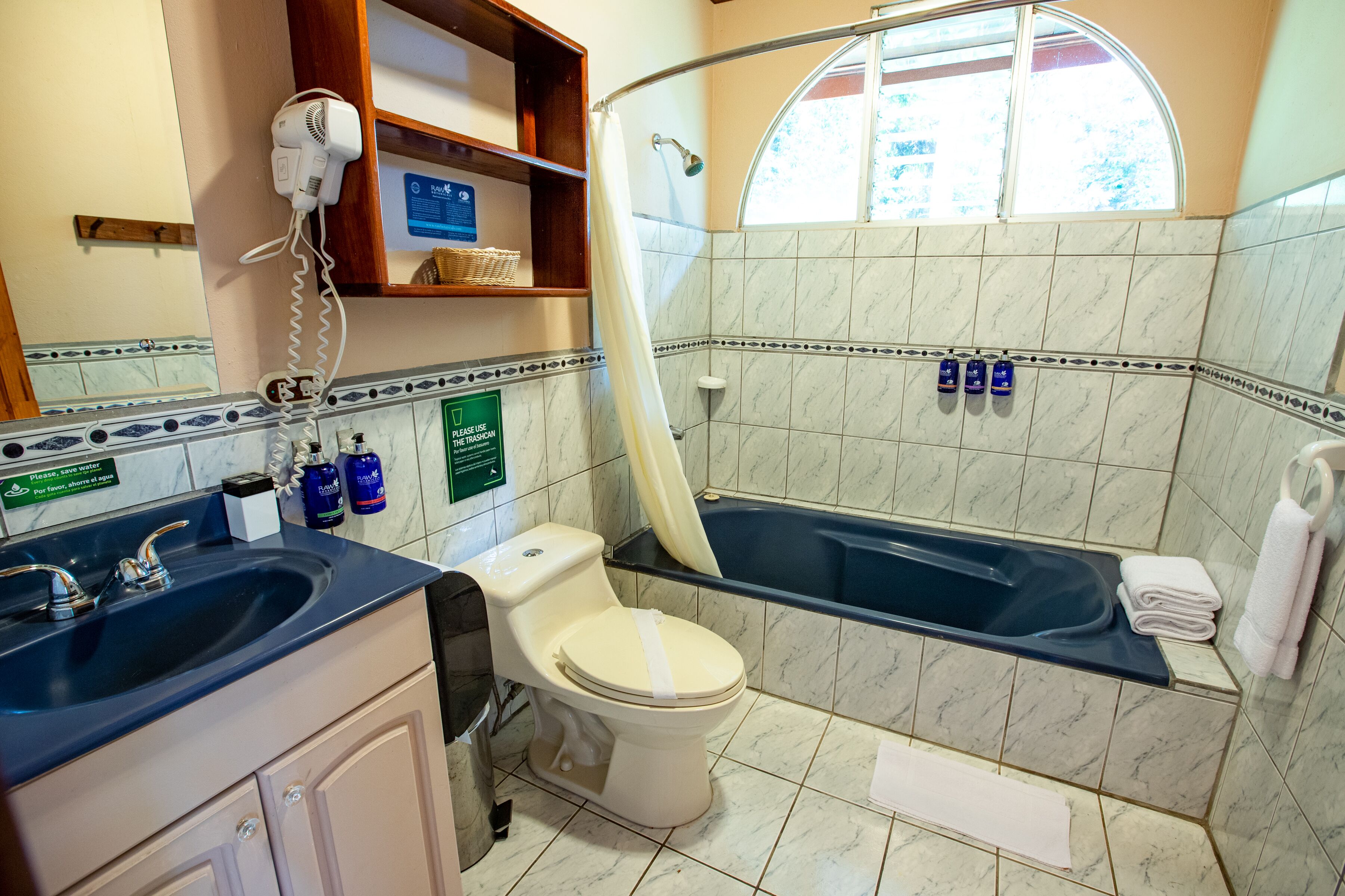 A bathroom with a sink, toilet, and bathtub. There is a shower curtain, a hairdryer, and toiletries on the counter.