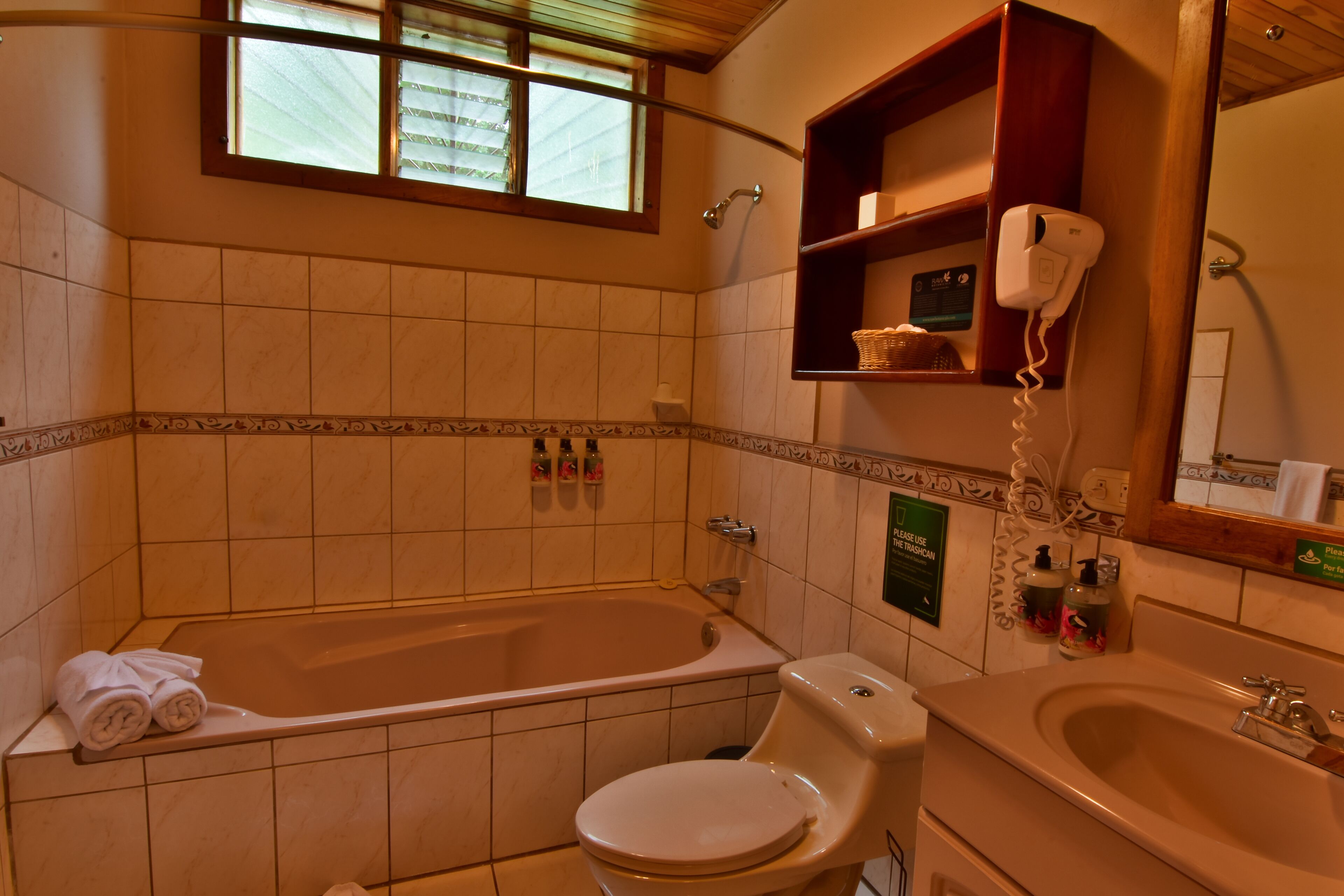 A bathroom with a bathtub, toilet, and sink. There are towels on the tub, a hand dryer, and a shelf with toiletries.