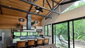 Cozinha moderna com área de refeições, grandes janelas e um espaço de estar acolhedor com sofá e cadeiras.