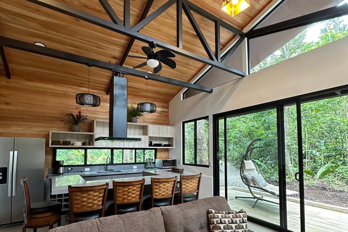 A modern kitchen with a dining area, large windows, and a cozy seating area with a sofa and chairs.