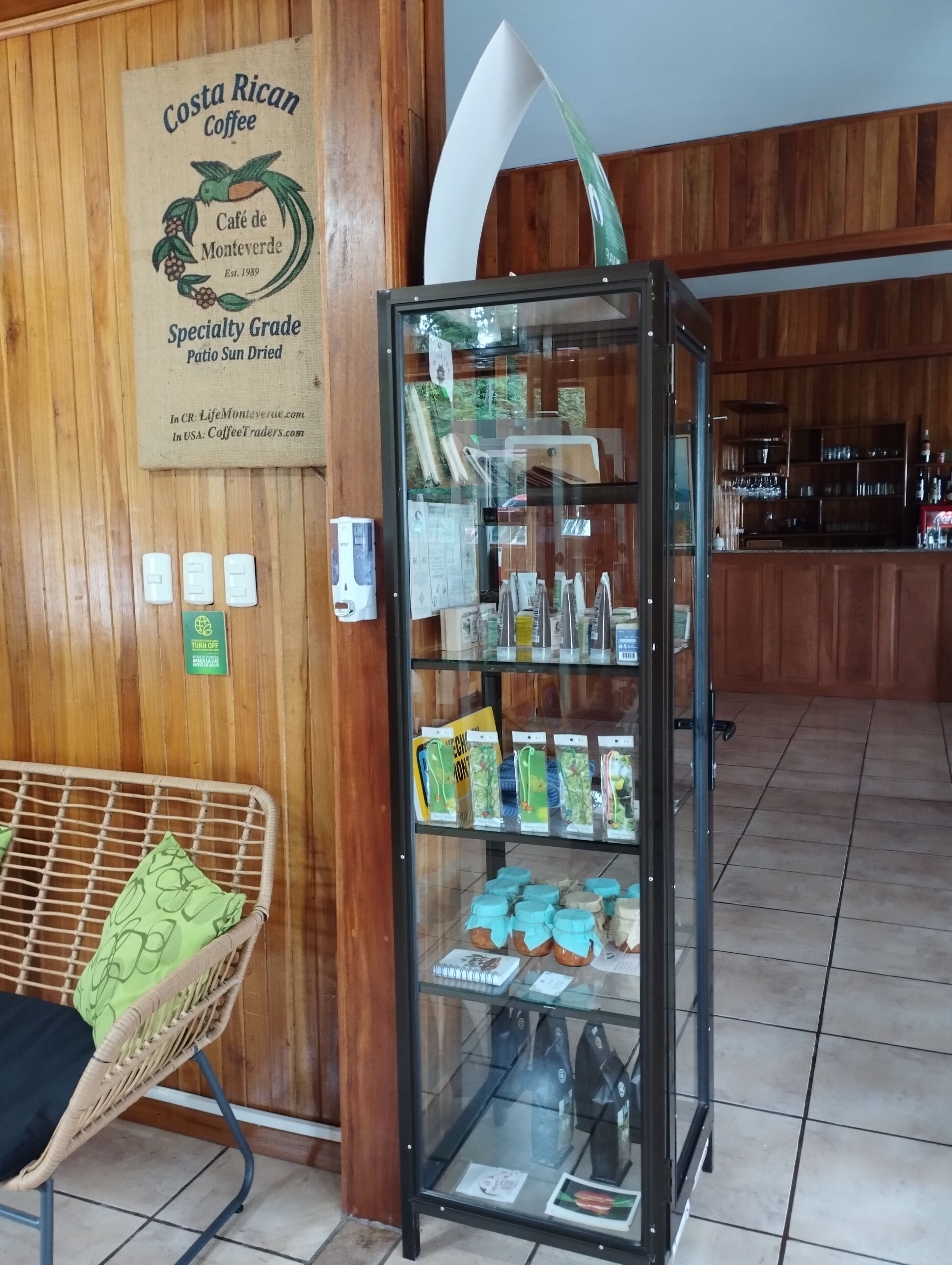 A Costa Rican Coffee Café de Monteverde with a glass display case containing coffee products and a wicker chair.