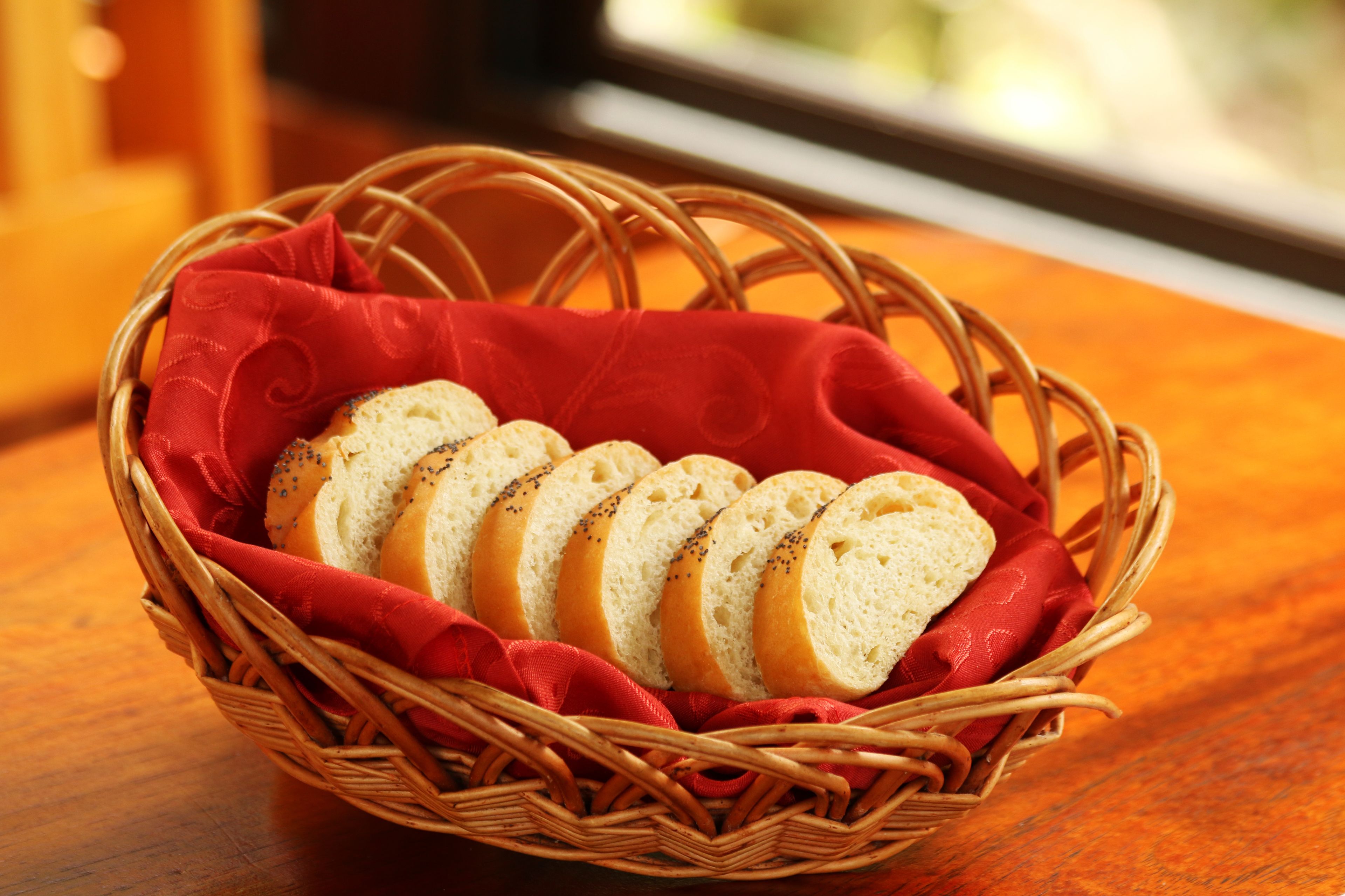 A wicker basket containing sliced bread with poppy seeds on a wooden table.