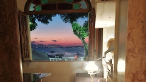 Een kamer met uitzicht op zee bij zonsondergang, een klein rond tafeltje en een lamp.