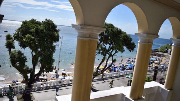 Uitzicht vanaf een balkon op een strand met parasols en mensen.