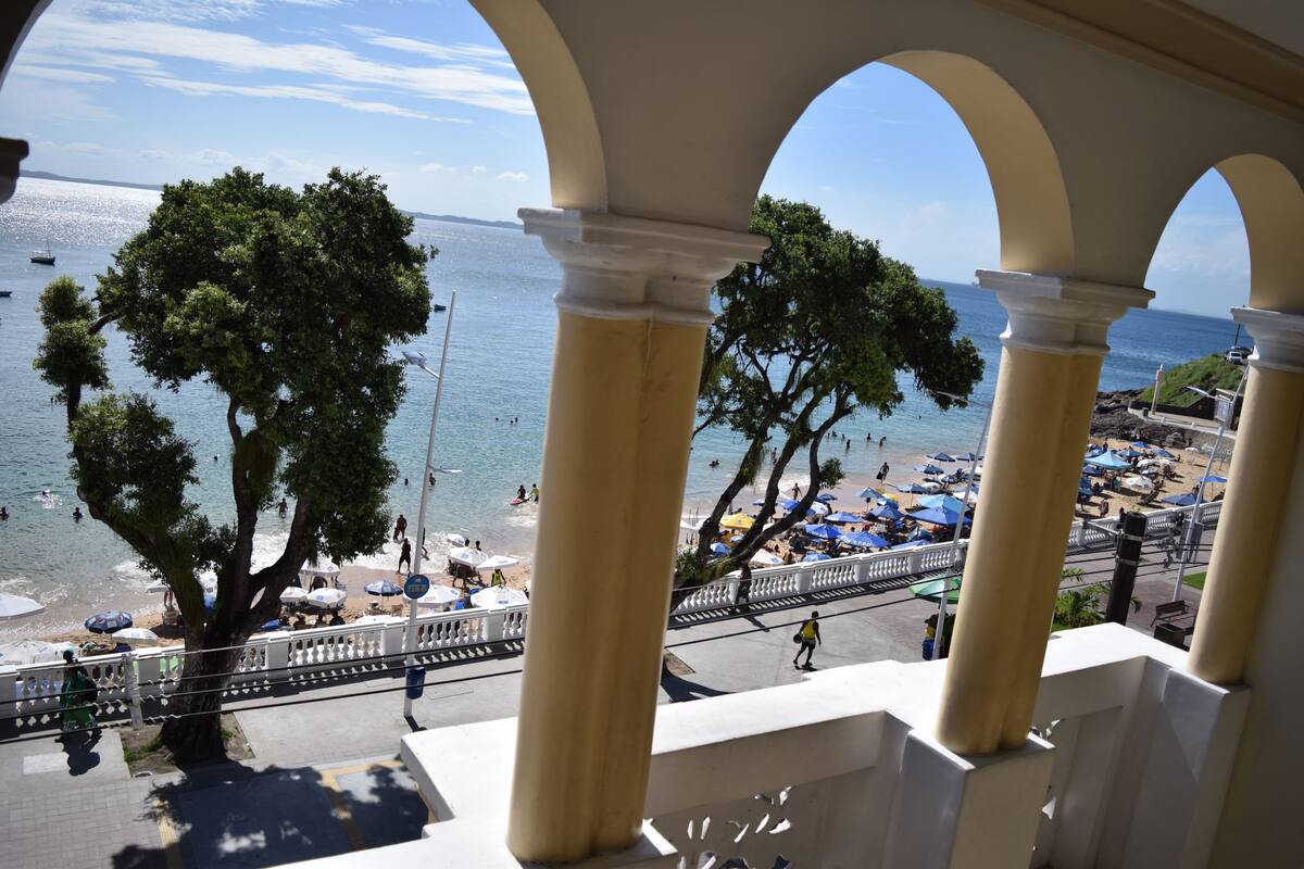 Blick vom erhöhten Balkon auf einen Strand mit Sonnenschirmen und Menschen.