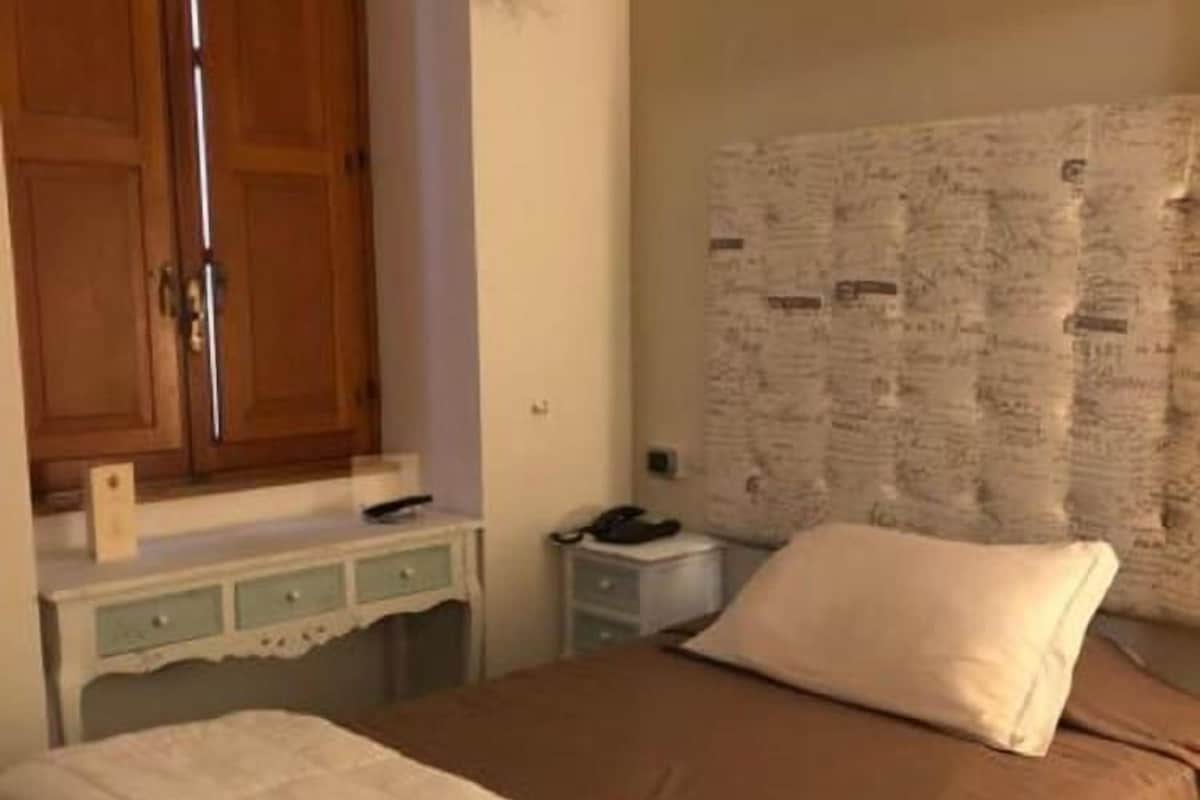 A bedroom with a bed, a wooden wardrobe, a small bedside table, and a wall with a bulletin board.