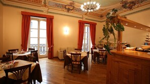 A dining area with wooden tables and chairs, large windows with red curtains, and a chandelier. - Hotel Medici (Milazzo)