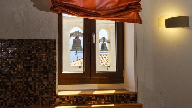 A bathroom with a mosaic-tiled wall, a window with a curtain, a bathtub, and a wall-mounted light fixture. - Hotel Medici (Milazzo)