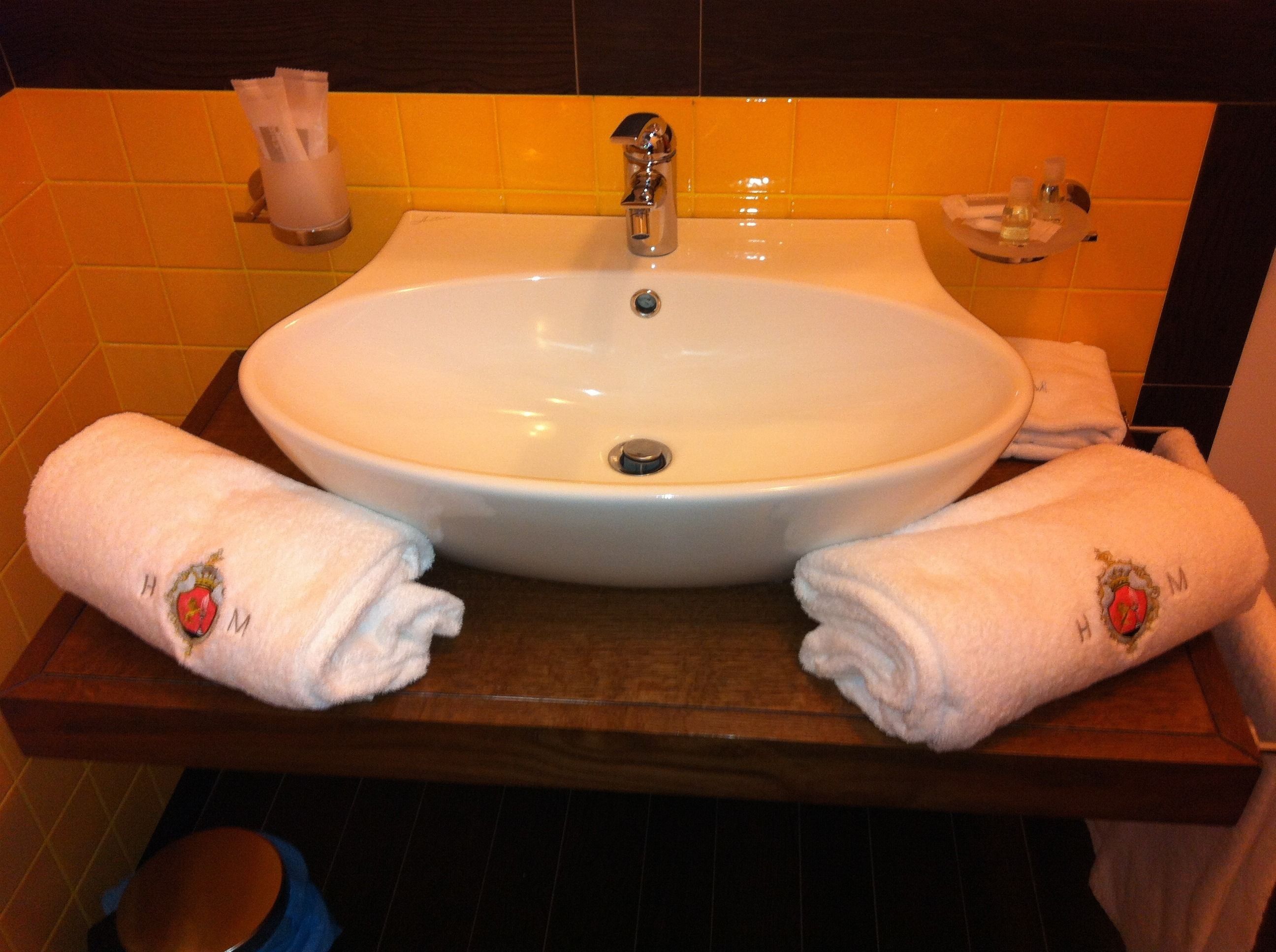 A bathroom with a white sink, two towels with embroidered logos, and a soap dish.