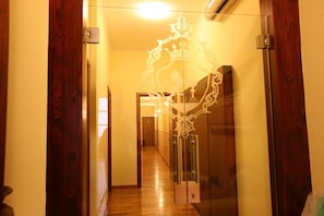 A hallway with wooden flooring, a glass door with a decorative pattern, and a light fixture on the ceiling. - Hotel Medici (Milazzo)