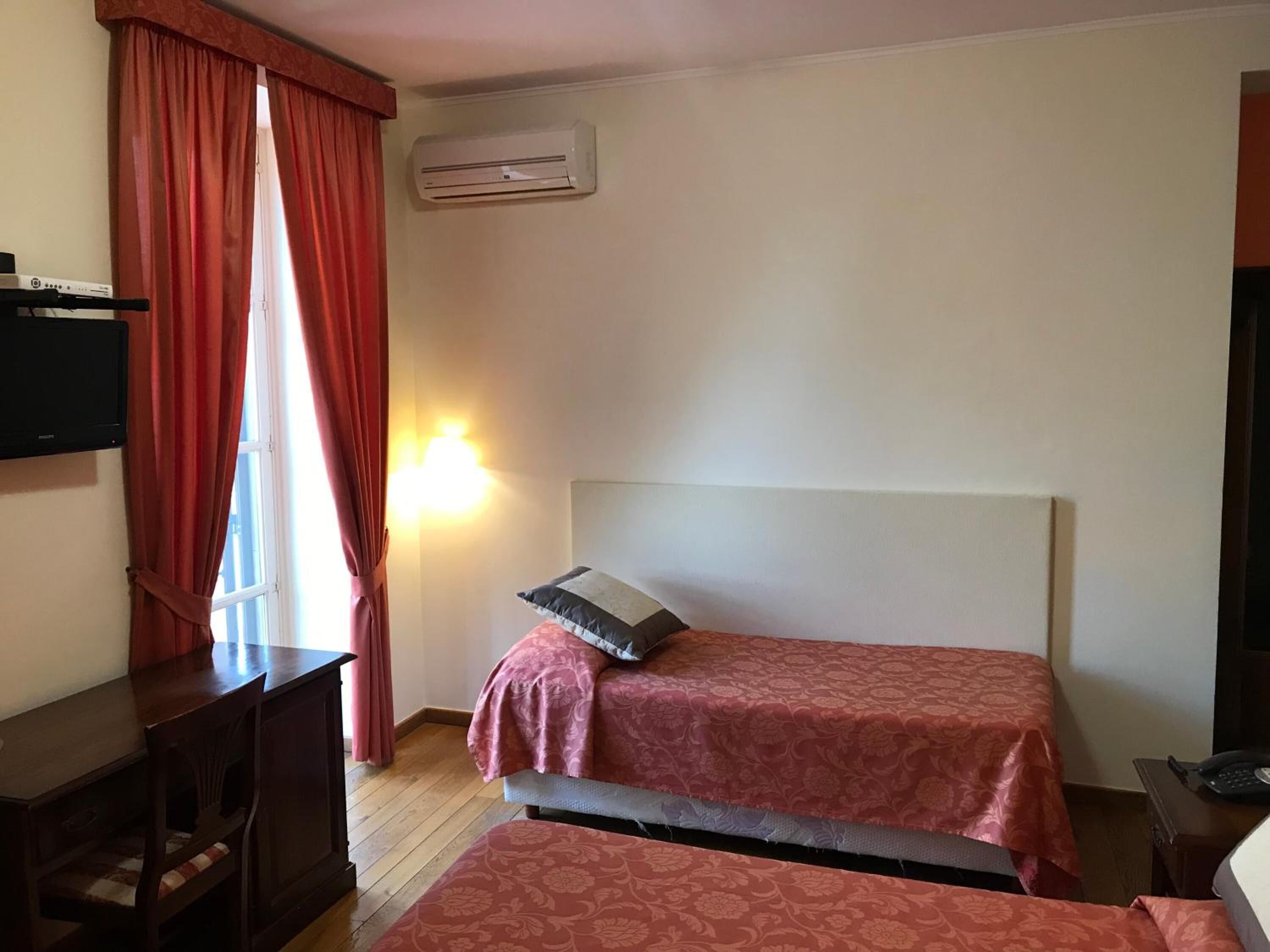 Ein Zimmer mit zwei Betten, einem Schreibtisch, einem Fernseher und einer Klimaanlage.