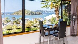 Una habitación con un ventanal grande que ofrece vistas a la costa, una mesa de comedor con sillas y un ventilador de pie.