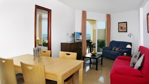 A living room with a wooden dining table, a red sofa, and a television on a wooden cabinet. - Apartamentos Euromar Playa (Torrox)