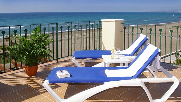 A terrace with two lounge chairs and a table, a potted plant, and a view of the sea. - Apartamentos Euromar Playa (Torrox)