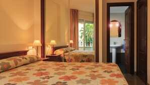 A hotel room with a bed, two bedside tables with lamps, a large mirror, and a view of the balcony with plants. - Apartamentos Euromar Playa (Torrox)