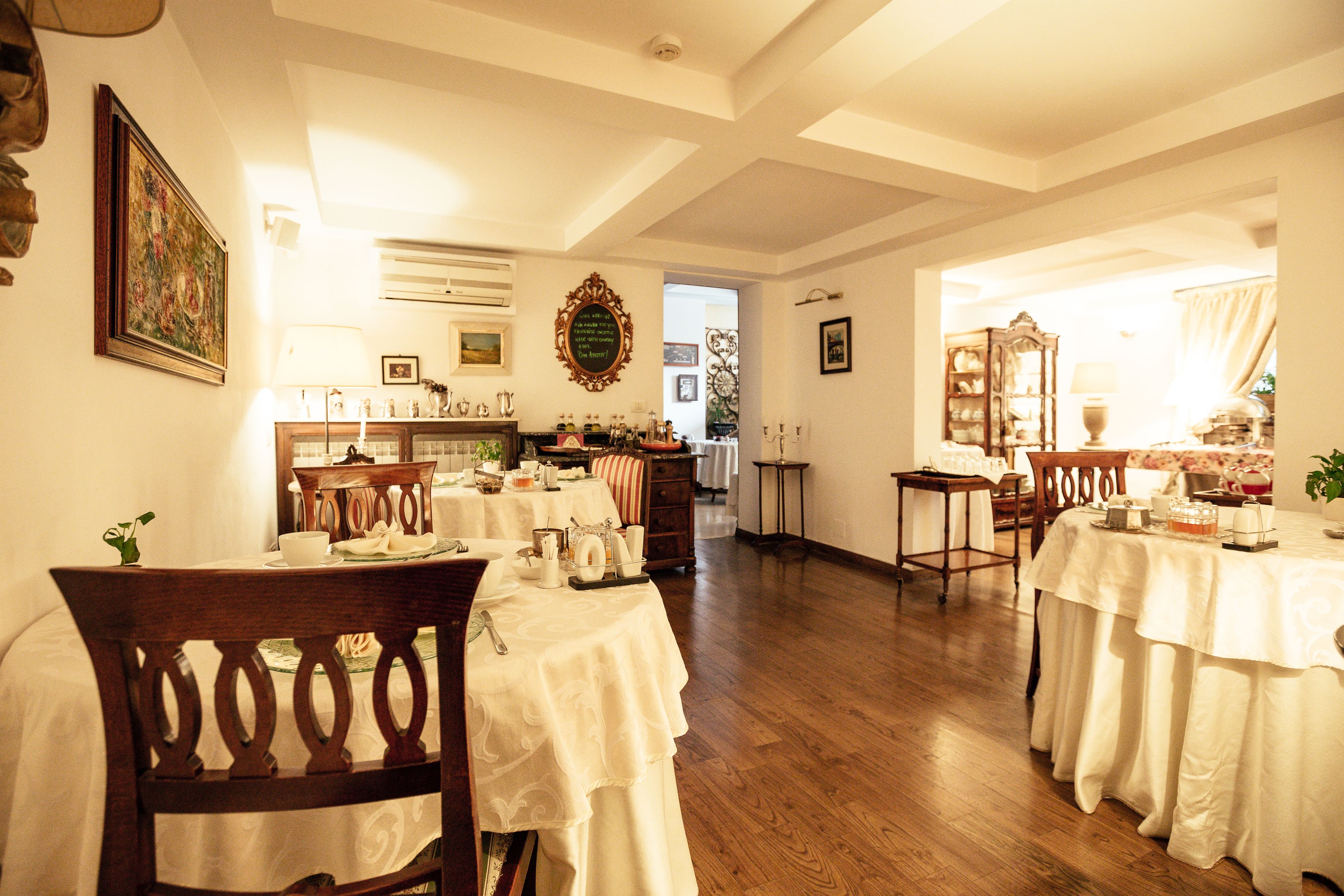 A dining area with multiple tables set for a meal, wooden chairs, and a chandelier.
