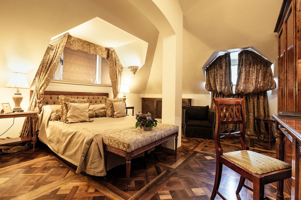 A bedroom with a four-poster bed, a wooden chair, a desk, and a large mirror.