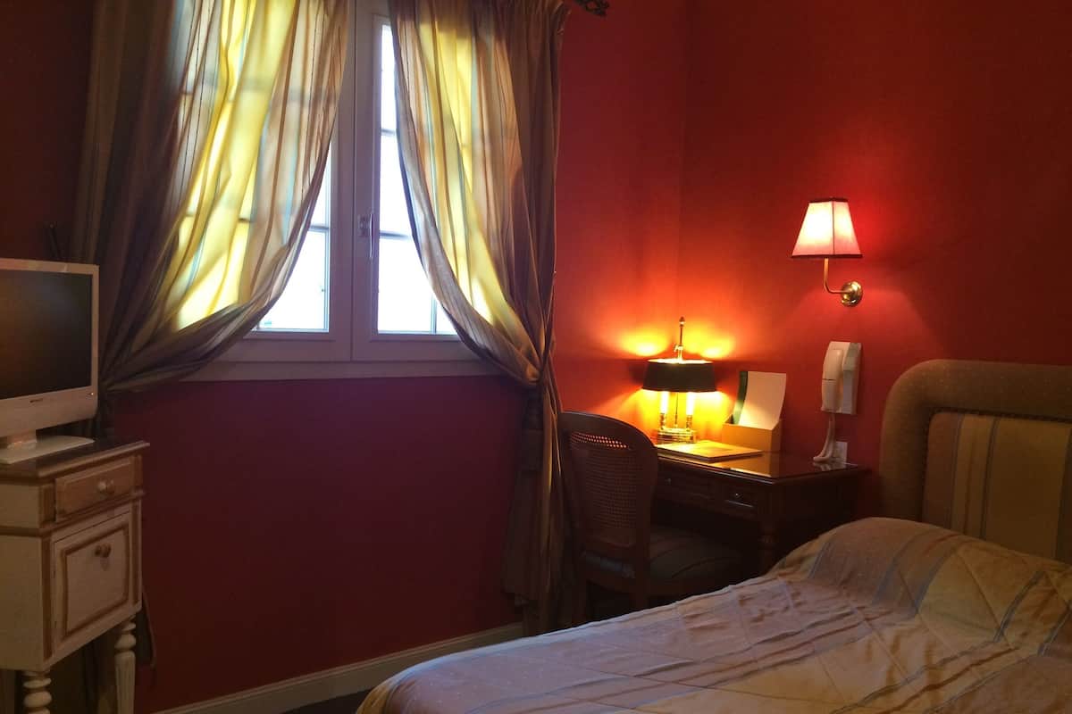 A hotel room with a bed, a desk with a lamp, a chair, a television, and a telephone.