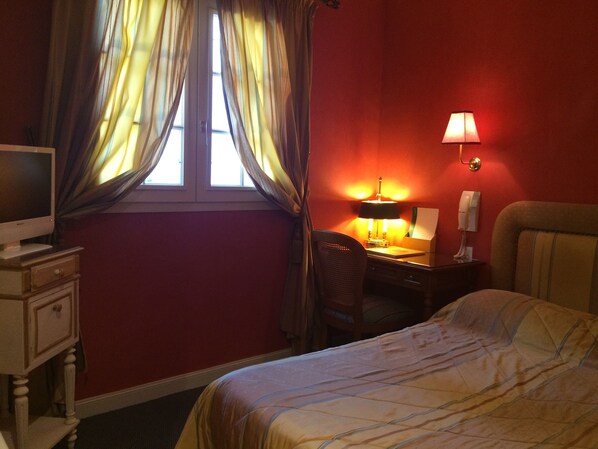Una habitación de hotel con cama, escritorio con lámpara, silla, televisor y teléfono.