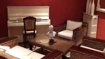 A room with a piano, wicker furniture, and a decorative painting on the wall.