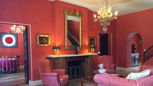 Un salon aux murs rouges, avec une cheminée, un lustre et un escalier.
