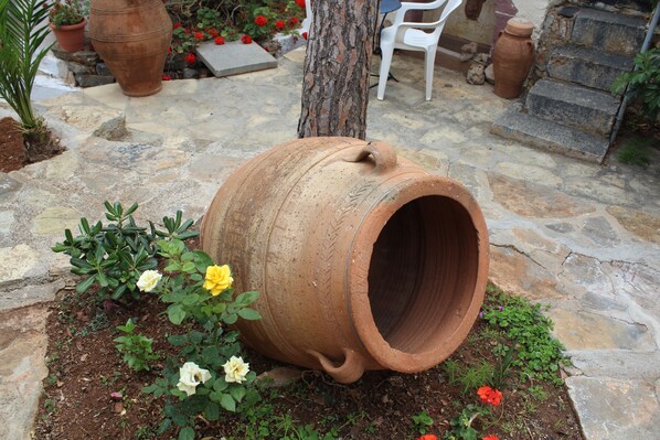 En rustik utomhusmiljö med en stor terrakotta-kruka, omgiven av olika växter och blommor.