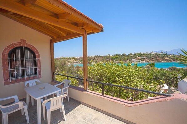 A balcony with a table and chairs, overlooking a coastal landscape with buildings and a clear sky.