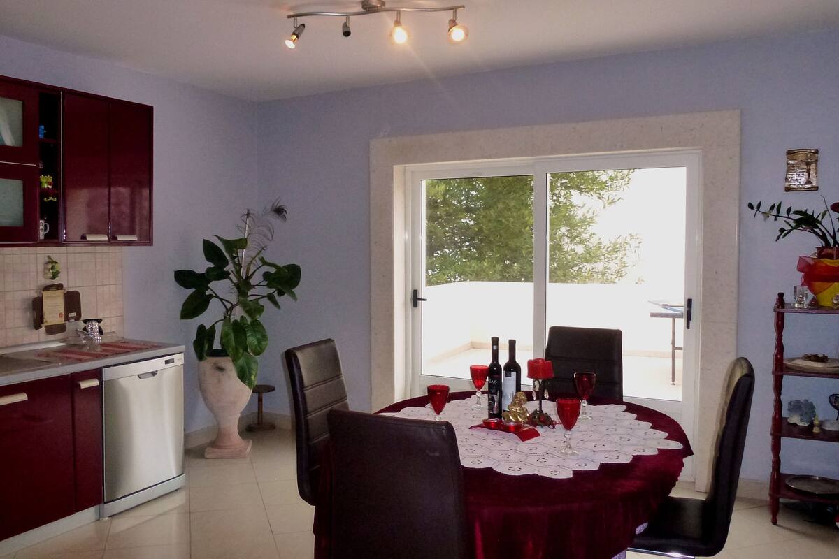 A kitchen with a dining area, a large window, and a potted plant.